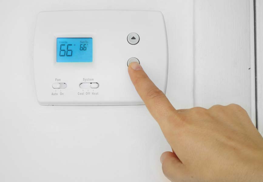 Person's hand adjusting a wall mounted thermostat temperature
