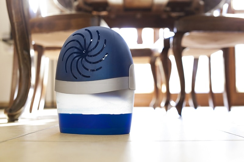 Close up of a blue and white dehumidifier placed on a dining room floor
