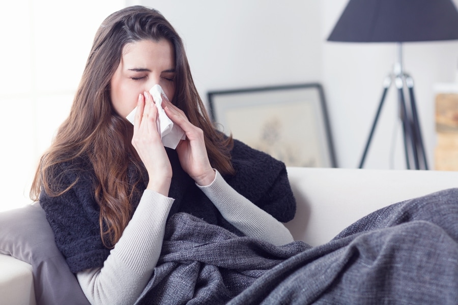 Woman blowing her nose from allergies due to poor indoor air quality in her home .