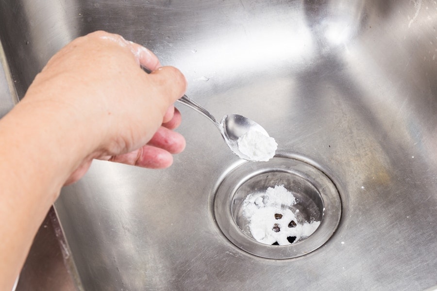 Homeowner pouring baking soda down the kitchen sink after learning how to help unclog a drain.