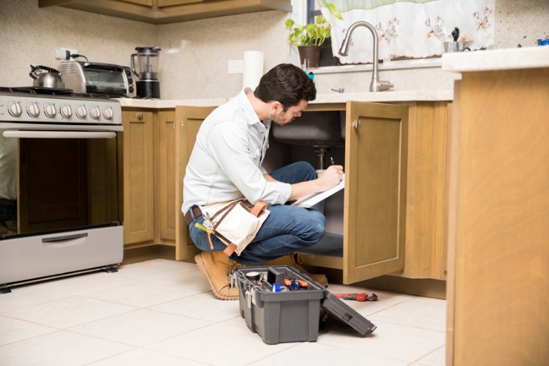 Do I Need a Plumbing Inspection? Image is a photograph of a male HVAC professional working on a kitchen sink.
