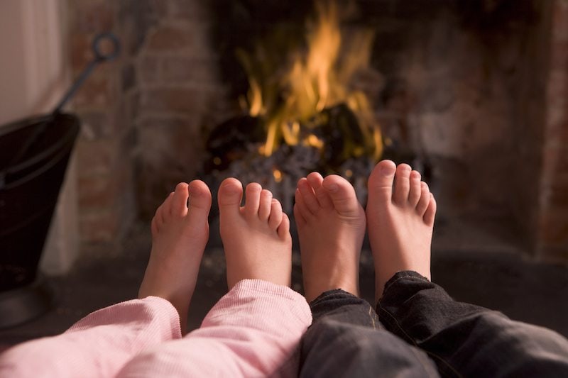 Children's feet warming at a fireplace sitting down in living room: A heating decision needs to be made: heat pump or furnace?
