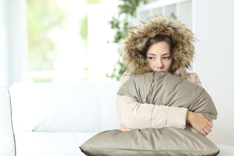 Angry woman warmly clothed in a cold home sitting on a couch.
