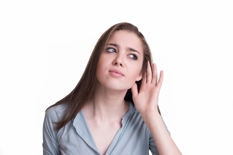 Portrait of concerned young girl with hand to ear gesture carefully listening gossip