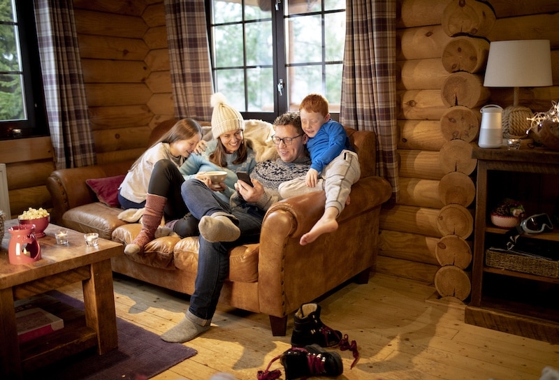 A family relax on the sofa in a log cabin and use a smartphone.