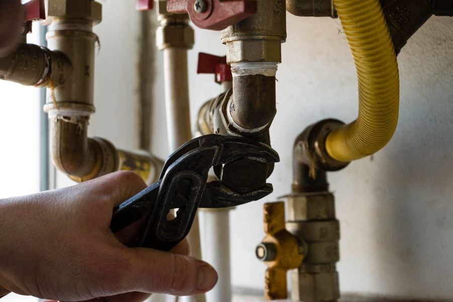 Everything You Need to Know About Boilers. Image shows a hand holding a wrench and working on pipes.
